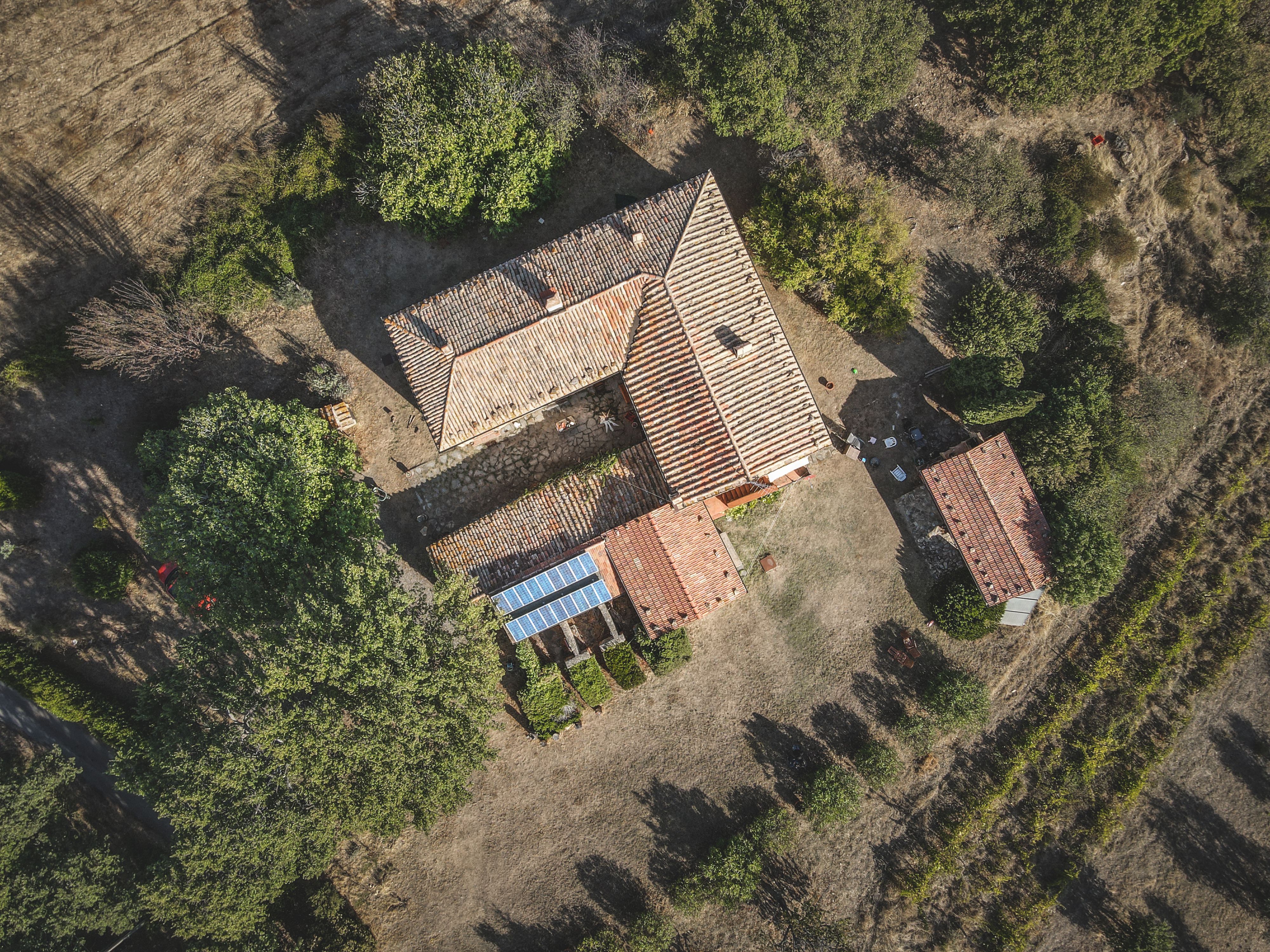 Aerial shot of a rustic farmhouse surrounded by greenery in a rural setting.