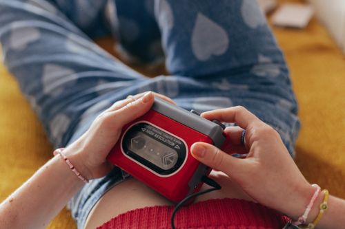 Free Close-up of hands holding a red cassette player, wearing heart-pattern jeans, embodying a retro aesthetic. Stock Photo