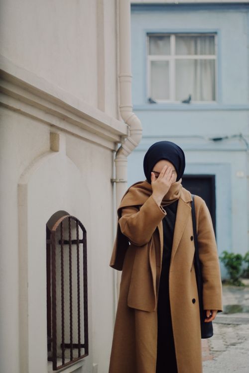Free A woman in a hijab covers her face with her hand while standing on a city street. Stock Photo