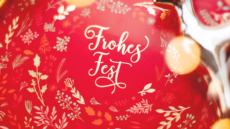 A vibrant red Christmas card decorated with delicate golden patterns and a festive message.