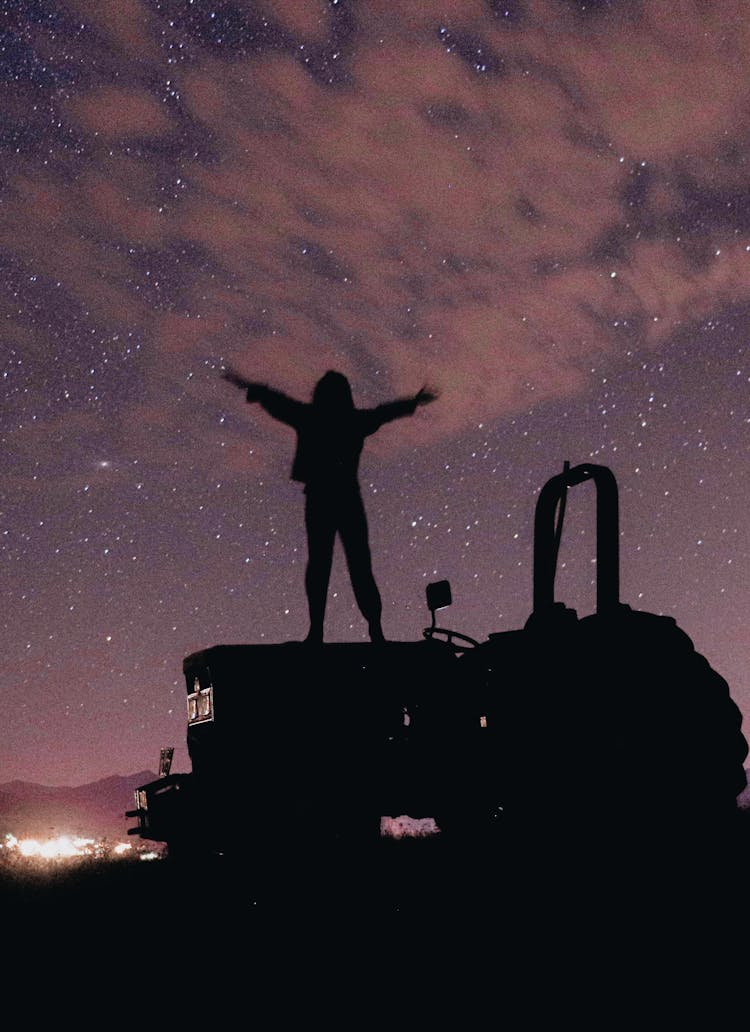 

A Silhouette Of A Person Standing On A Tractor Under A Starry Sky