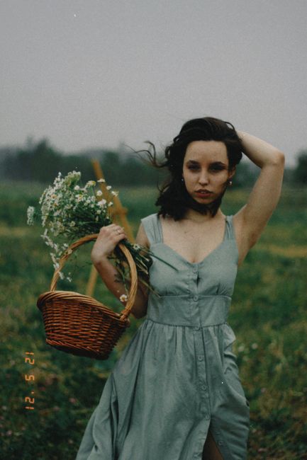 A woman in a flowing dress carries a basket of flowers in a scenic Almaty field.