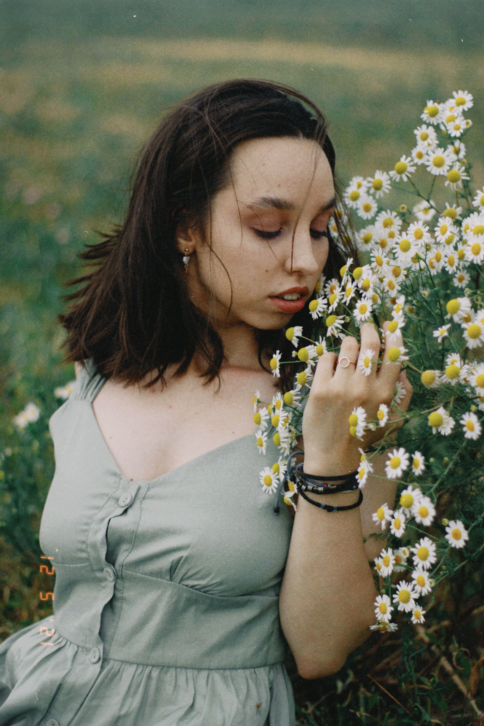 A young woman in a green dress enjoys chamomile flowers in a lush meadow.