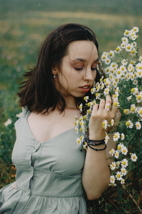 Girl Sitting on the Meadow and Smelling Chamomile Flowers
