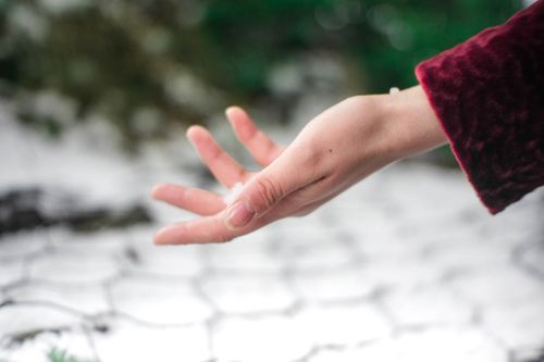 Free A close-up of a person's hand reaching out over a snowy background, suggesting cold winter vibes. Stock Photo