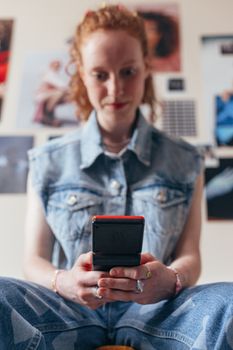 Young woman in denim using a retro handheld device in a cozy indoor setting.