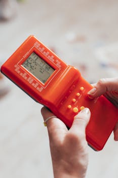Close-up of hands playing a retro handheld game console, evoking nostalgia.