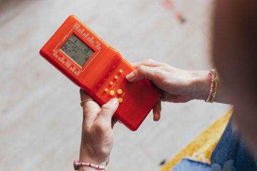Hands holding a retro red handheld game console, playing a classic game.