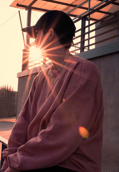 Free Stylish person in pink sweater and black cap sitting, with sunlight creating a dramatic sunburst effect. Stock Photo