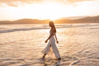 一位穿着飘逸连衣裙的女子在宁静的日落海滩漫步，捕捉到宁静