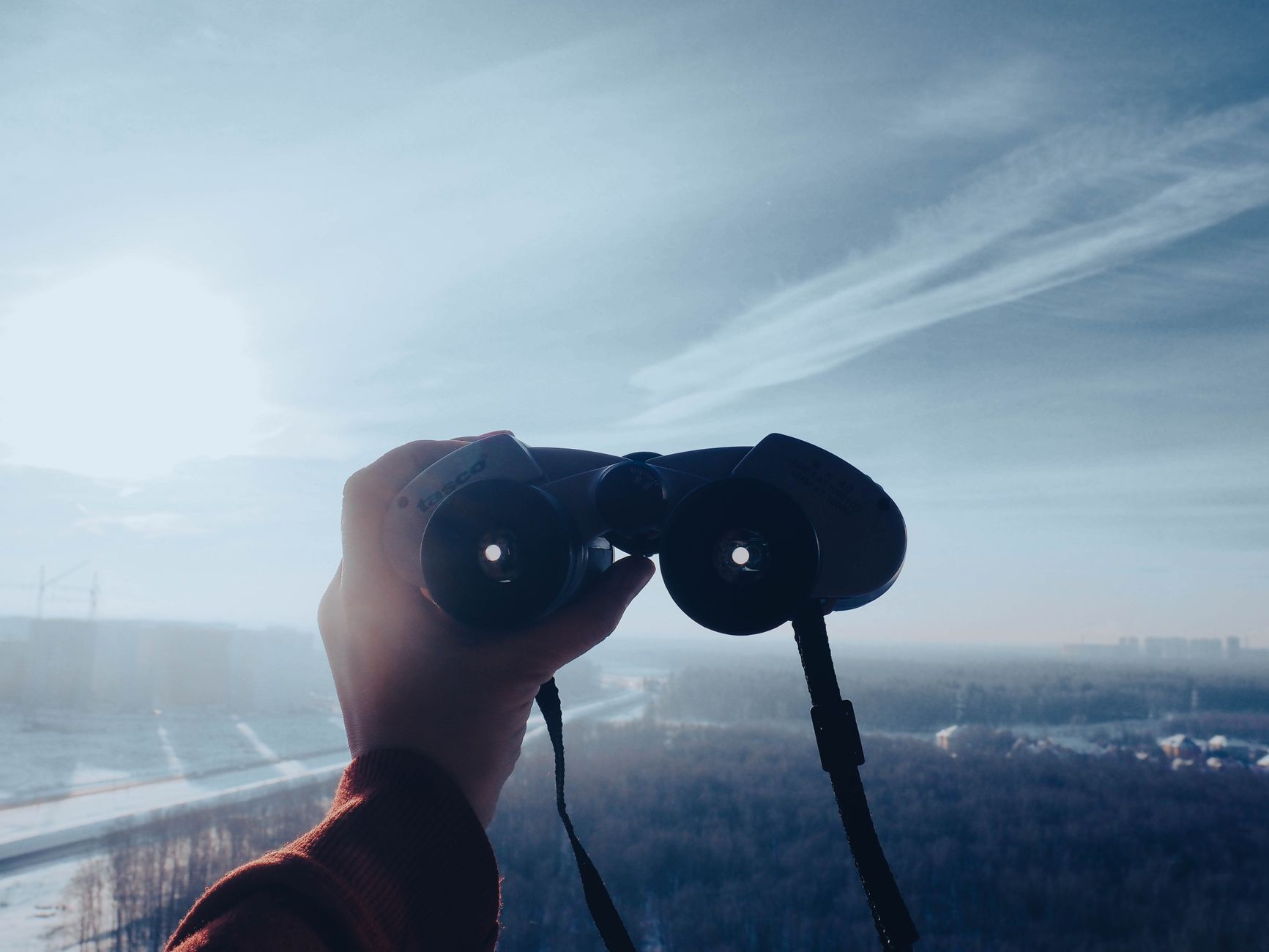 A hand holds binoculars toward a scenic horizon under a clear sky, capturing adventure and exploration.