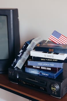 A retro setup with stacked VHS tapes and an American flag beside an old TV and video recorder.