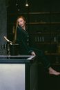 Blond Woman Sitting on Bar Counter and Looking at Cooled Bottle of Champagne