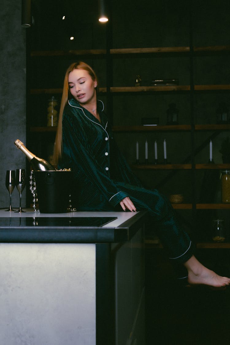 Blond Woman Sitting On Bar Counter And Looking At Cooled Bottle Of Champagne 