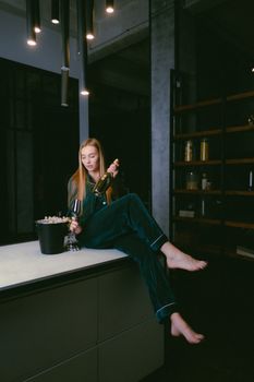 A woman in velvet pajamas holding a champagne bottle indoors. Elegant and relaxed setting.