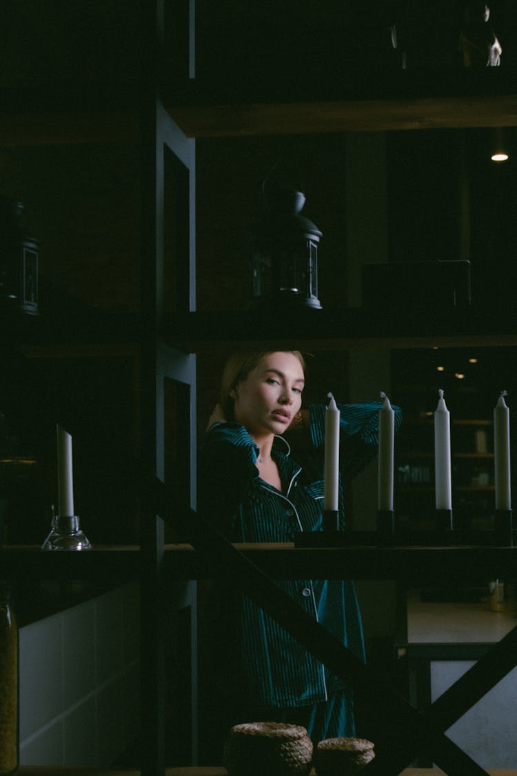 Young Woman Looking From Behind Shelves With Standing White Candles