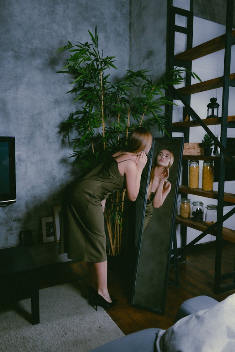 Blond Woman In Green Satin Dress And Black High Heels Looking At Reflection In Mirror