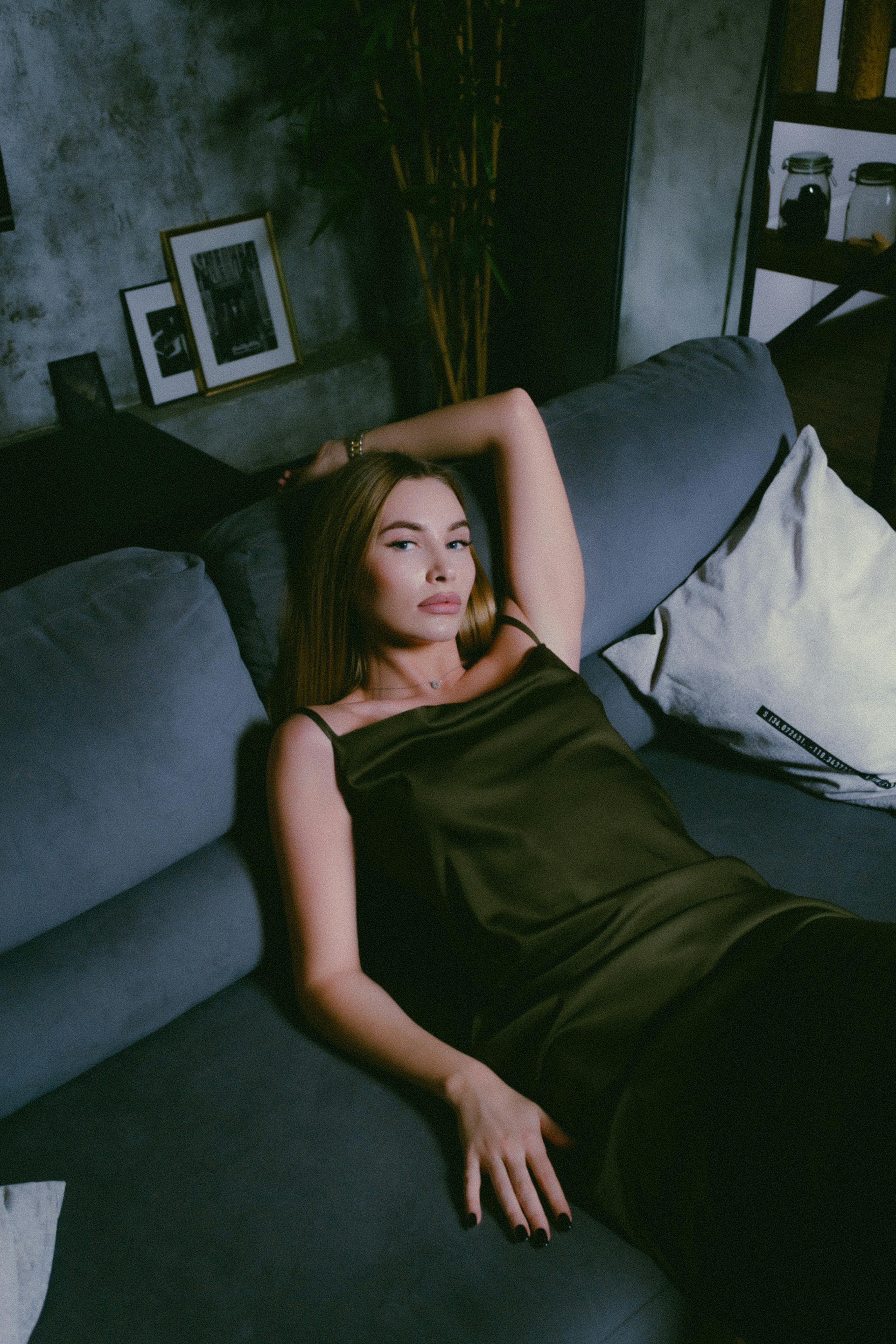 attractive young woman in green cocktail dress laying on sofa with hand on head