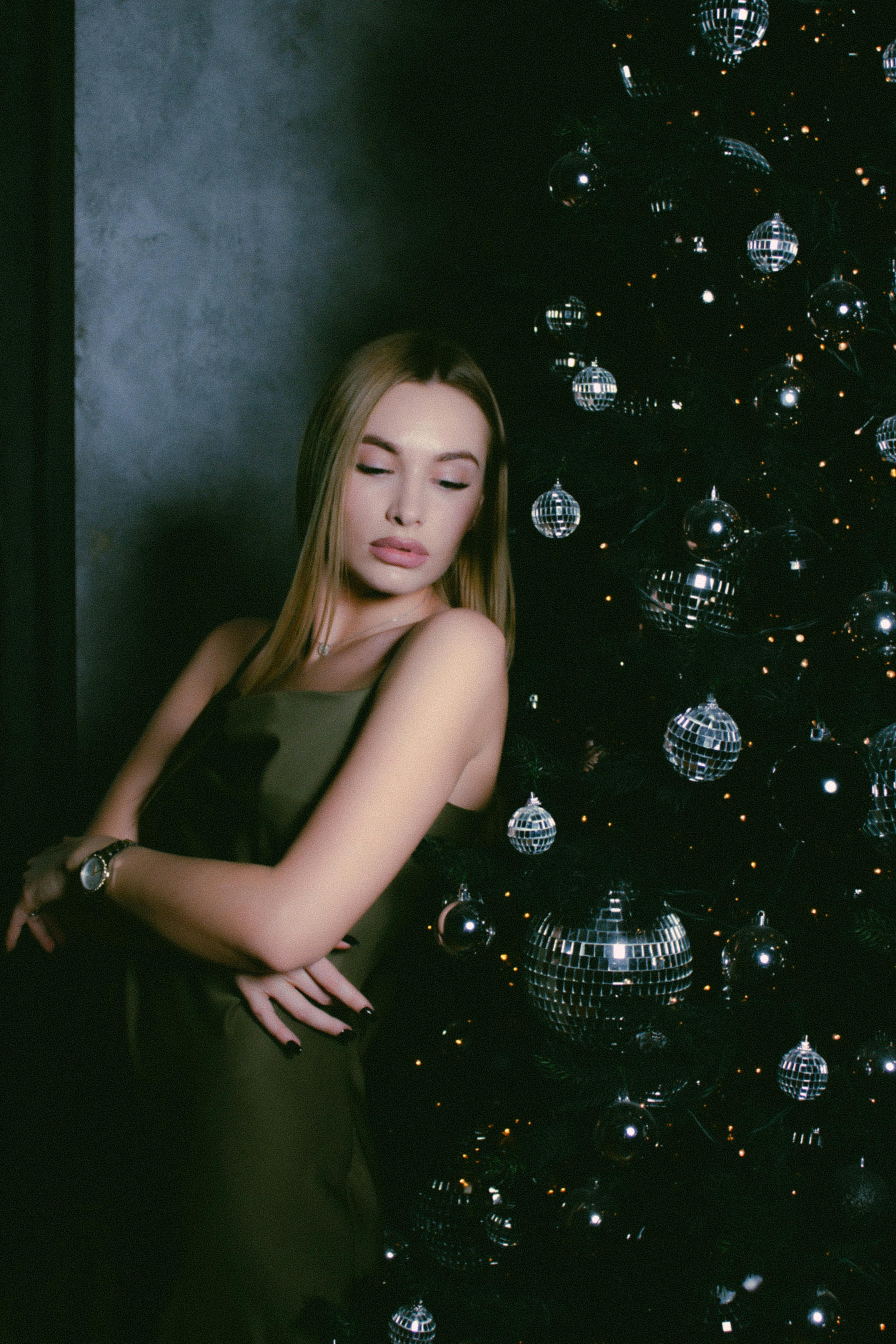 Young woman in a green dress posing beside an elegantly decorated Christmas tree indoors.