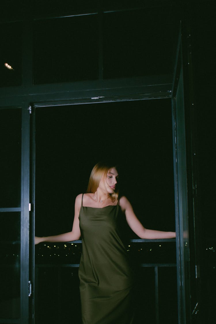 Blond Woman In Green Silk Dress Standing In Open Balcony Door At Night