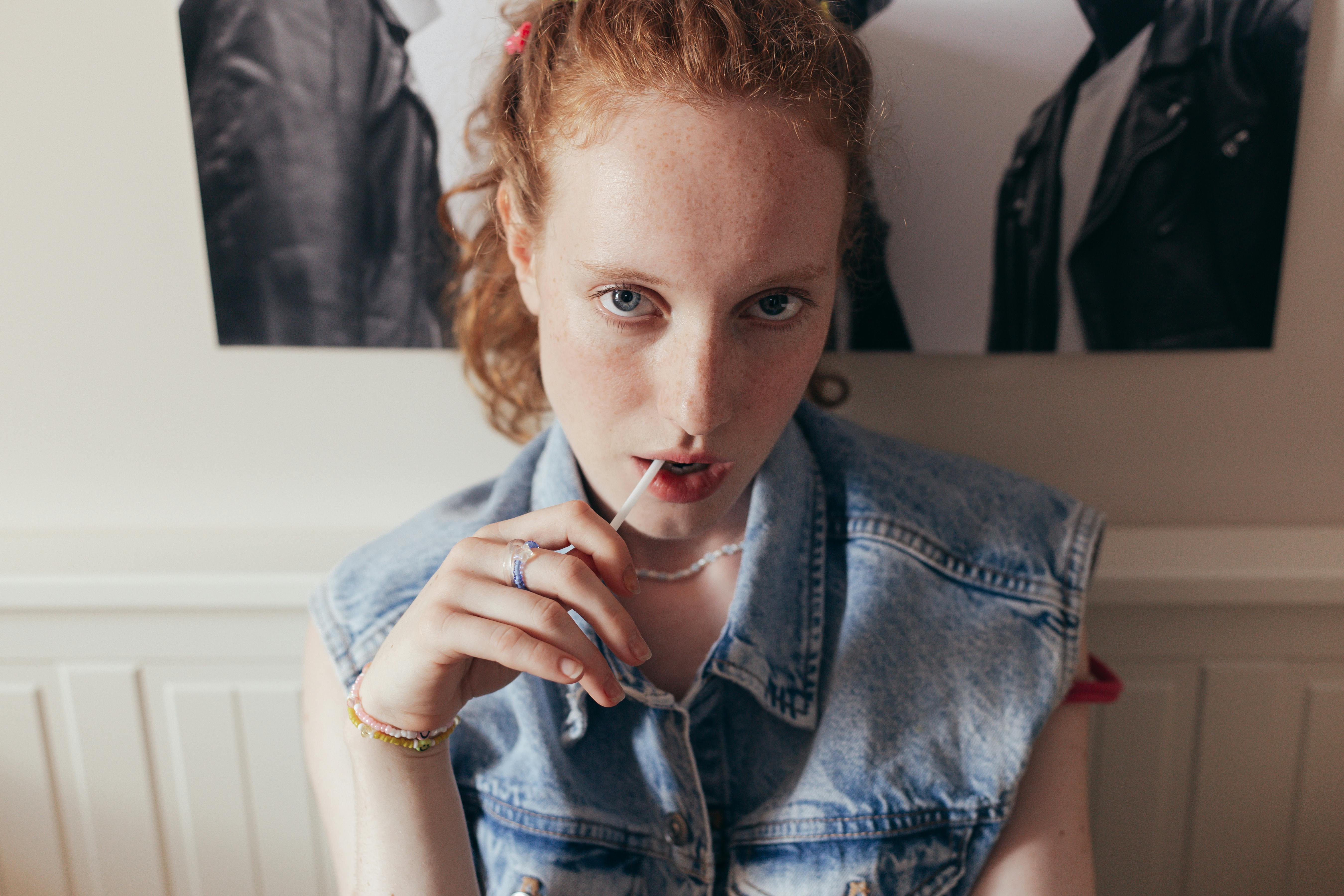 woman in blue denim vest eating lollipop