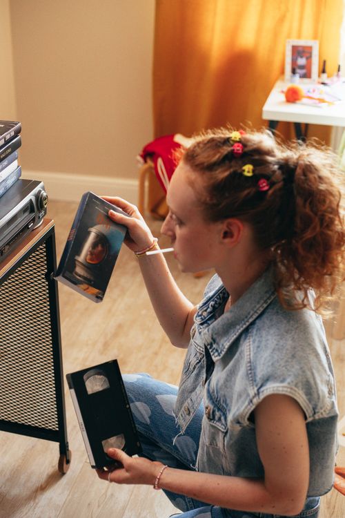 Free Woman enjoying nostalgic VHS tapes in a cozy indoor setting, reliving the 90s charm. Stock Photo