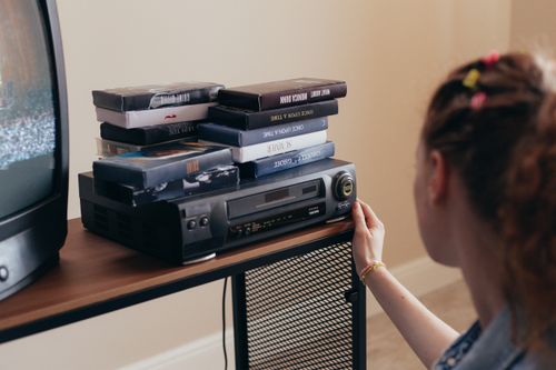 Free Young woman engaging with retro VHS tapes and a classic VCR setup. Stock Photo