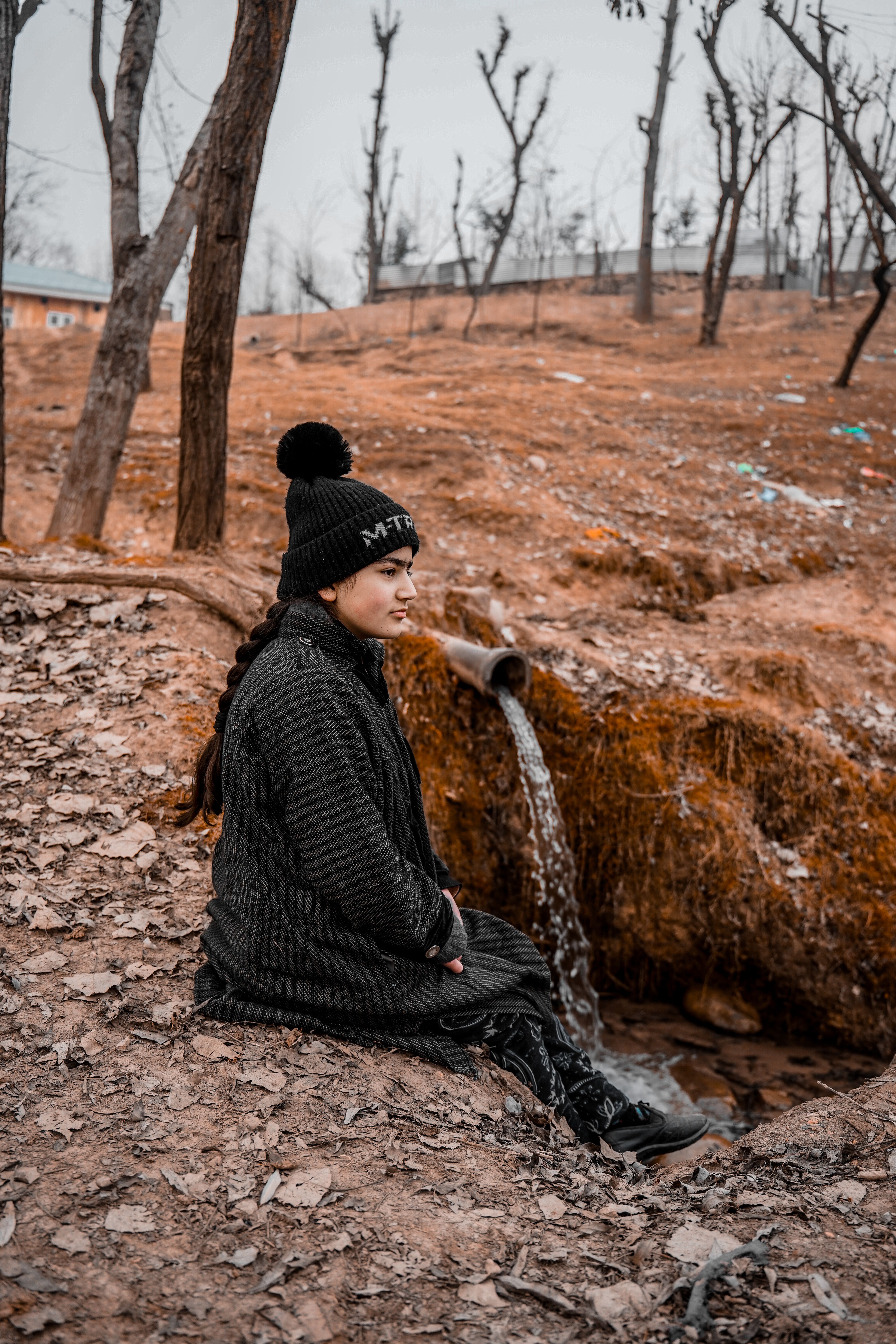 Young woman sitting by a stream in a quiet autumn forest setting.