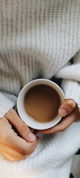 Close-up of hands holding a cup of coffee in a cozy sweater. Perfect for autumn vibes.