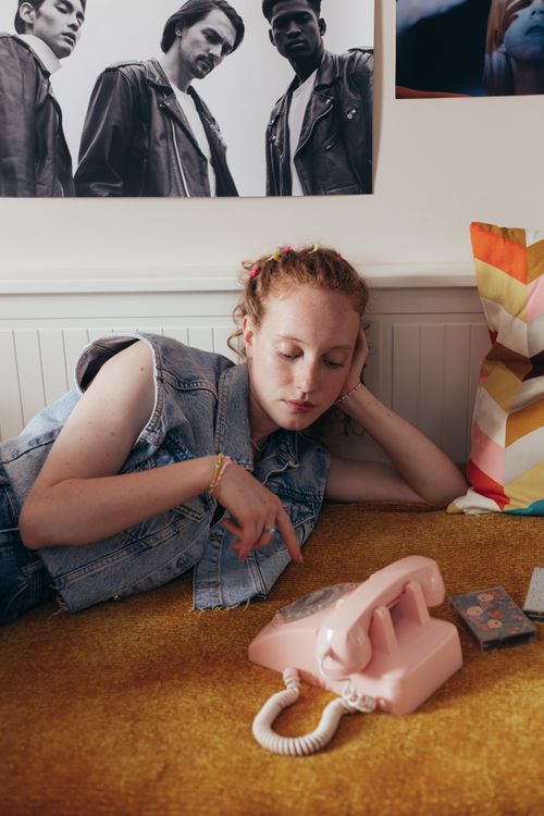 Free Young woman in denim lying on a bed using a vintage pink telephone. Stock Photo