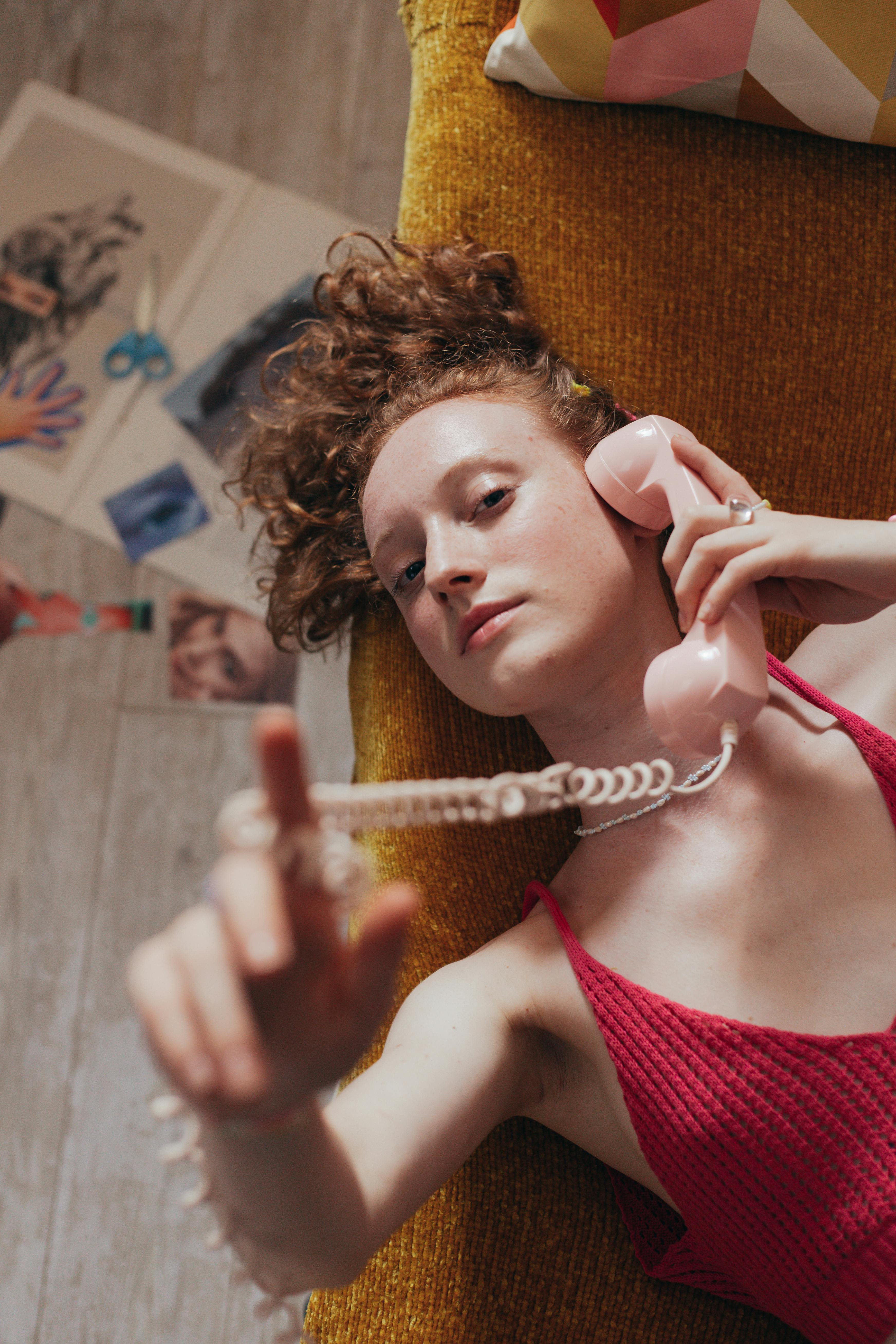 Young woman in red tank top using a retro rotary phone. Vintage 90s style portrait.