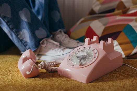 A nostalgic pink rotary telephone on a vintage carpet with jeans featuring heart patches.