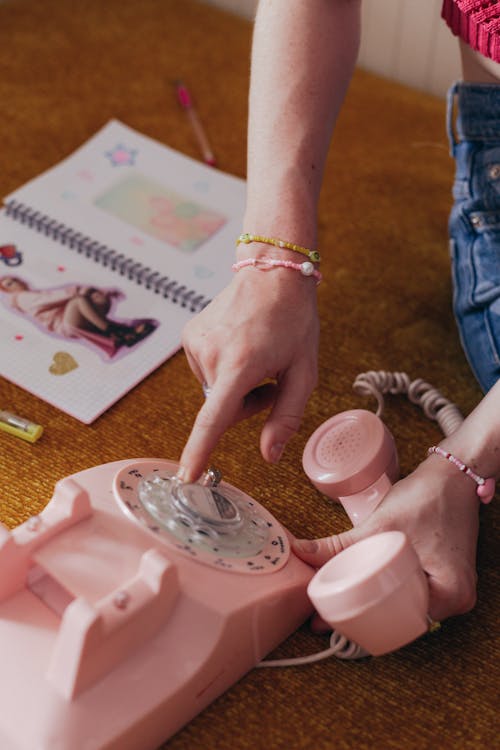 Photo of a Person's Hands Using a Pink Rotary Phone