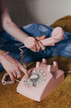 Close-up of a vintage pink rotary phone being dialed by a woman.