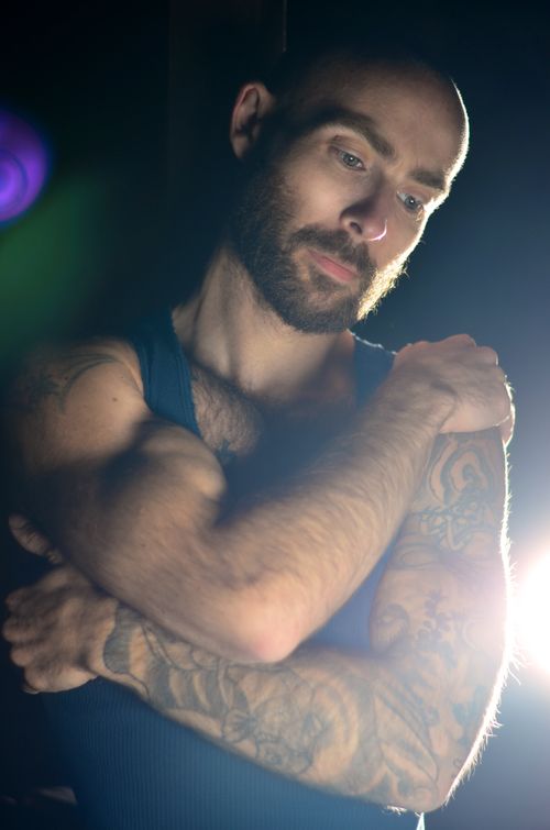 Free Dramatic portrait of a tattooed man embracing himself in dark ambiance. Stock Photo