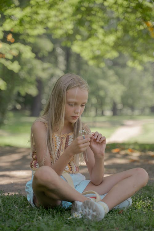 Free Girl Sitting on Grass and Playing with Flower Stock Photo