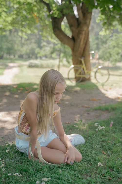 Free A young girl with long hair sits on the grass in a sunlit park, embracing summer. Stock Photo