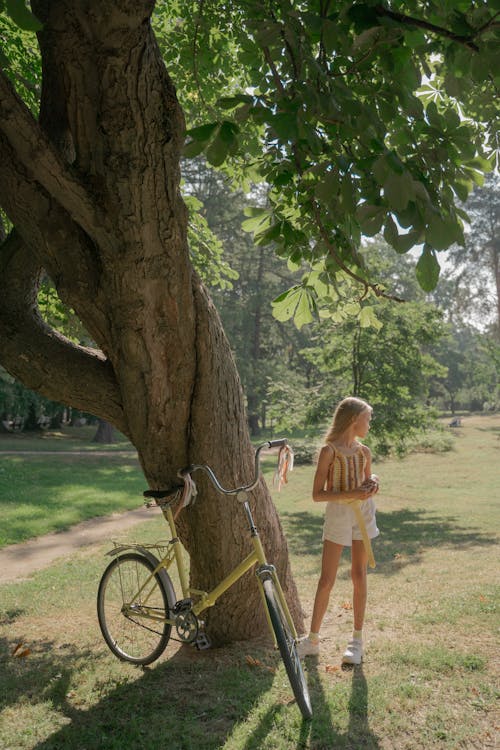 Free Girl Standing next to Tree and Bicycle Stock Photo