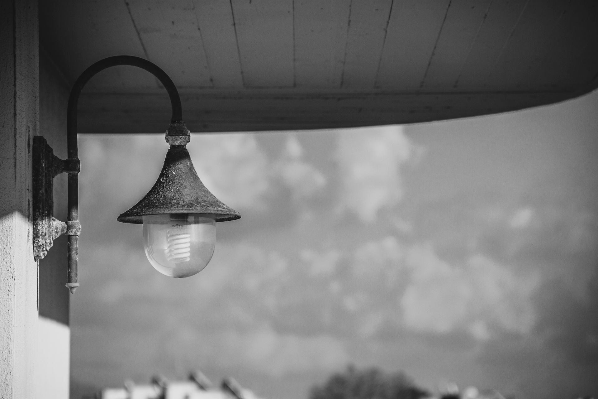Vintage lantern attached to a building with a cloudy sky backdrop in monochrome.