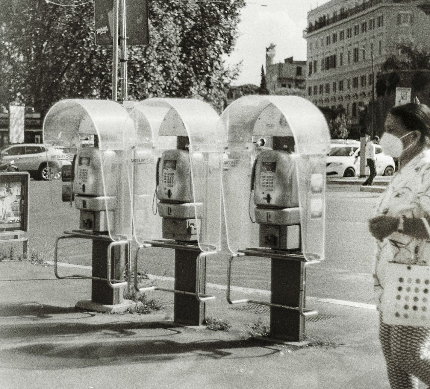 Black and white photo of three vintage public telephones on a city street with a passerby.