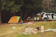 Explore a peaceful camping scene in the forest with a tent, car, and campfire setup.