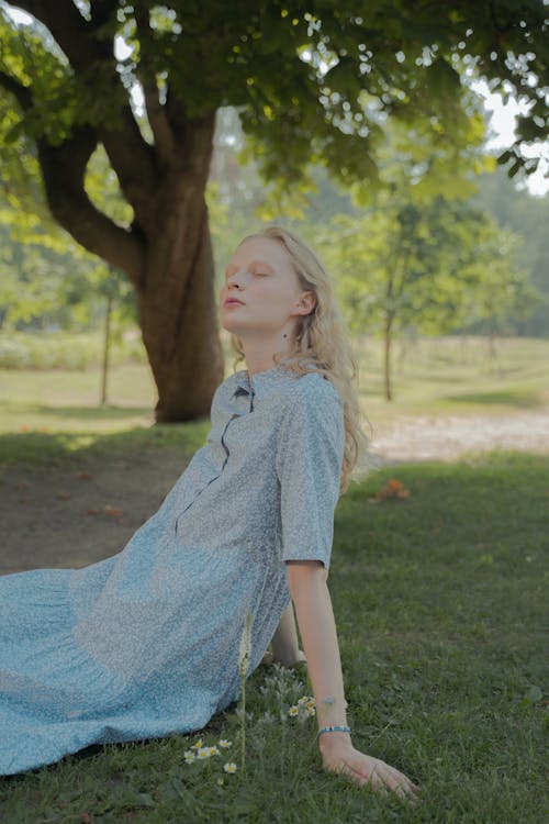 Blond Haired Teenage Girl in Dress Sitting on Grass with Eyes Closed
