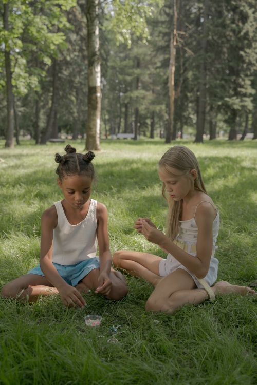 Free Two girls sitting on grass, enjoying a sunny summer day in a park. Stock Photo