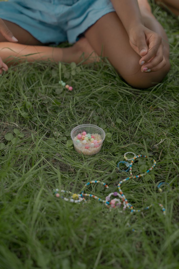 Girl Sitting On Grass Making Beads Necklace