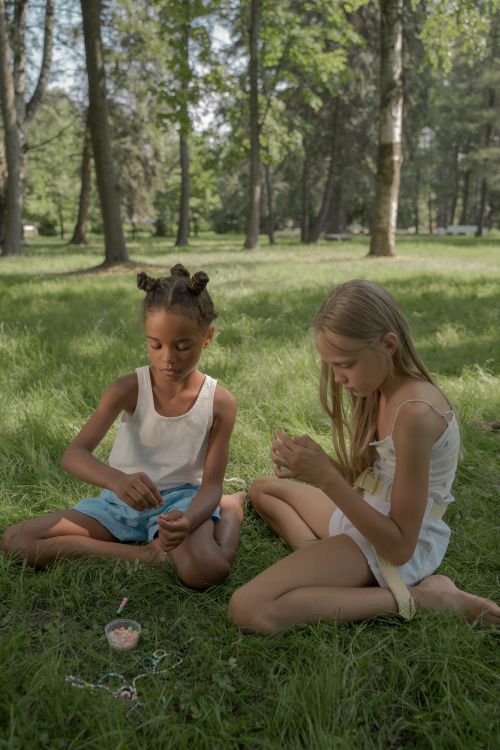 Free Two girls creating bead necklaces outdoors in a sunny park setting. Stock Photo