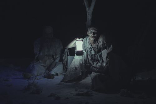 Free Performers in dramatic makeup and torn clothes gather around a lantern in a night outdoor setting. Stock Photo