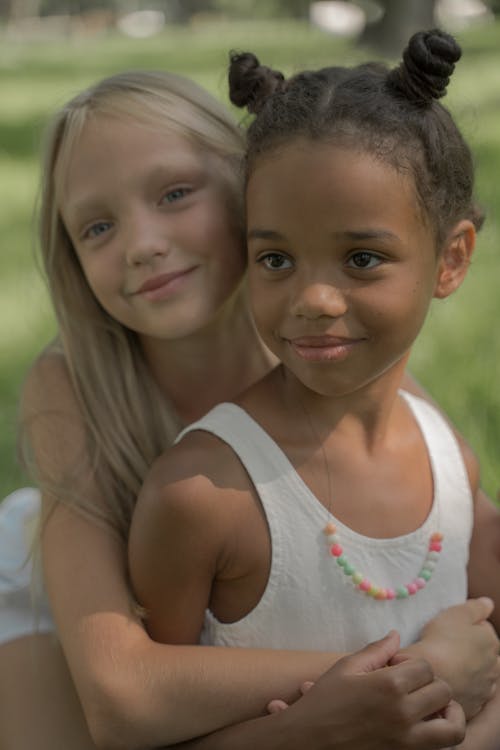 Cute Blond Girl Sitting Behind Other Teenage Girl and Embracing Her