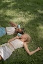 Two Girls Laying on Lawn and Playing Paper Cups Connected with String