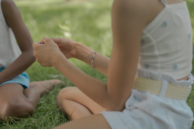 Girls Sitting On Grass Making Bracelets