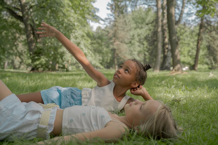 Girls Laying On Grass Pointing Up